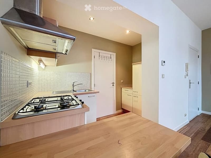 Modern kitchen with a gas stove, sink, wooden countertop, and cabinets. Features a range hood and recessed lighting.