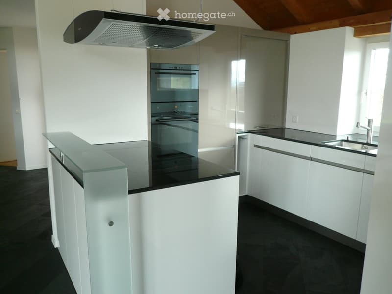 Modern kitchen with white cabinets, black countertops, stainless steel oven, and a range hood.