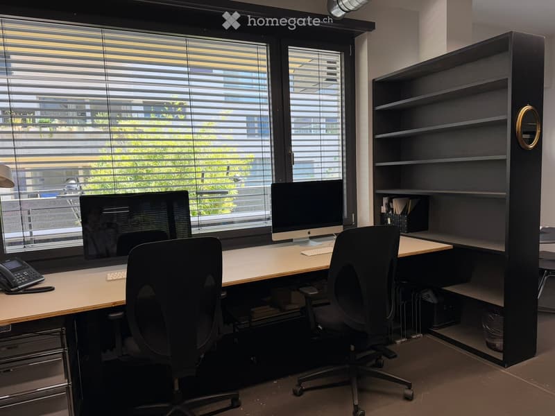 Modern office space with a large window, desk, ergonomic chair, computer monitor, keyboard, telephone, bookshelf, and a mirror.