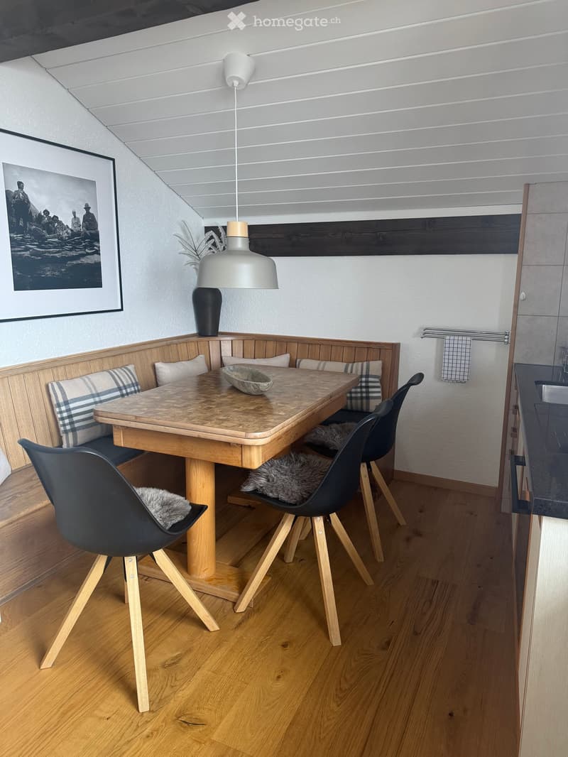 Dining area with a wooden table, black chairs, a built-in bench with cushions, a pendant light, and a decorative vase on the table.