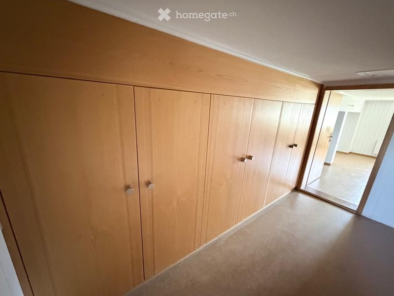 Empty hallway with light wooden built-in storage units and a smooth concrete floor, leading to an open doorway.