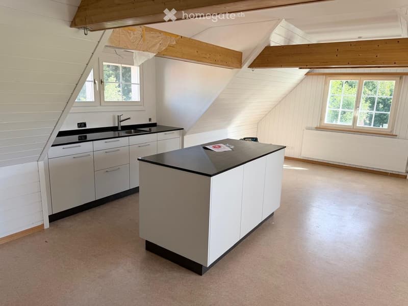 Modern kitchen with white cabinets, black countertops, and a central island. Features a sink with a modern faucet, large windows, and exposed wooden beams on the ceiling.