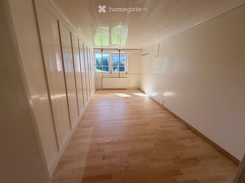 Empty hallway with wooden flooring, white walls, and large windows allowing natural light to enter.