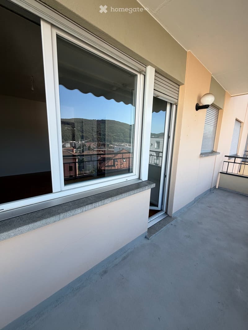 Balcony with large window, sliding glass door, concrete floor, and a view of the city and hills.