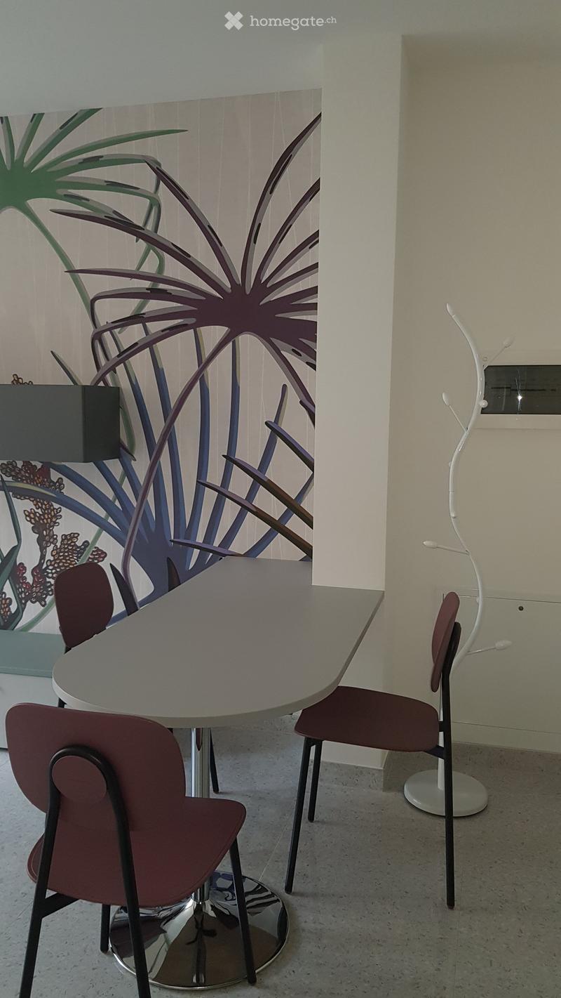 Modern dining area with a round table, four chairs, and a decorative lamp near a large abstract painting.