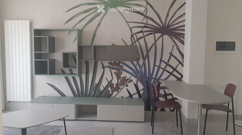 Modern, minimalist room with a large mural of a plant on the wall, featuring a grey table, chairs, and a grey shelving unit.