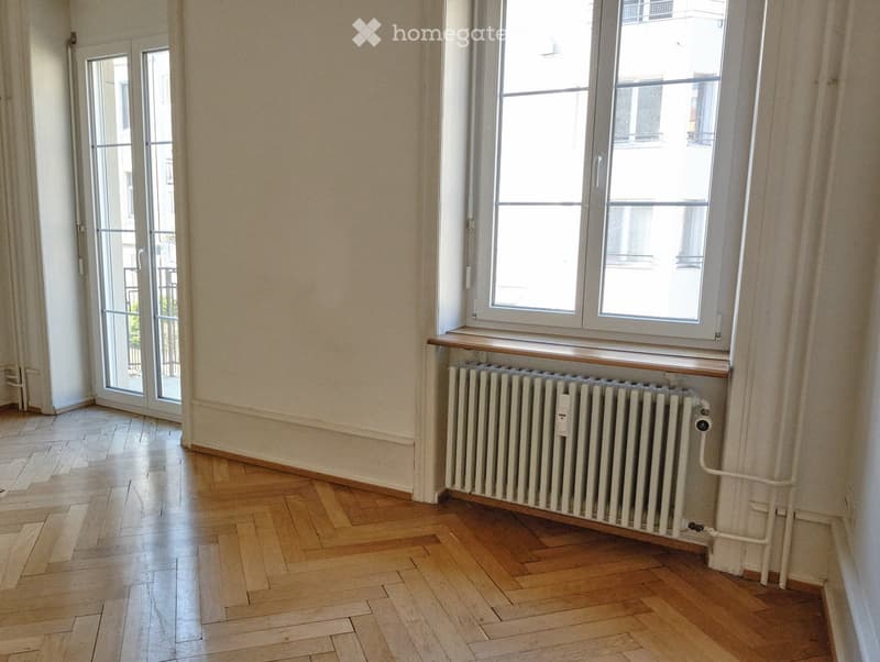 Empty room with wooden flooring, large windows, radiator, and sliding glass door leading to a balcony.