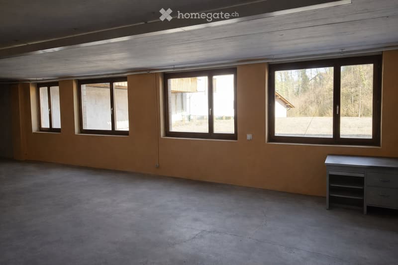 Empty room with concrete floor, large windows, and a small table in the corner.