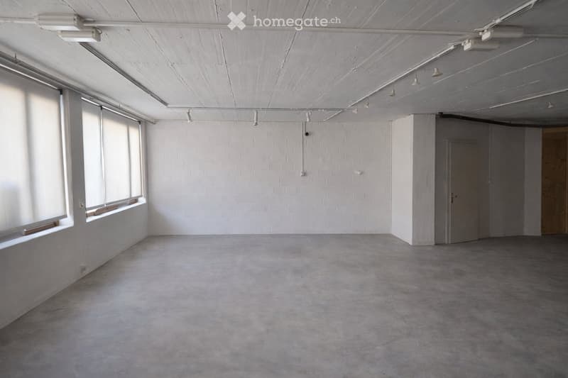 Empty room with white brick walls, large windows, and a concrete floor. No furniture or equipment is present.
