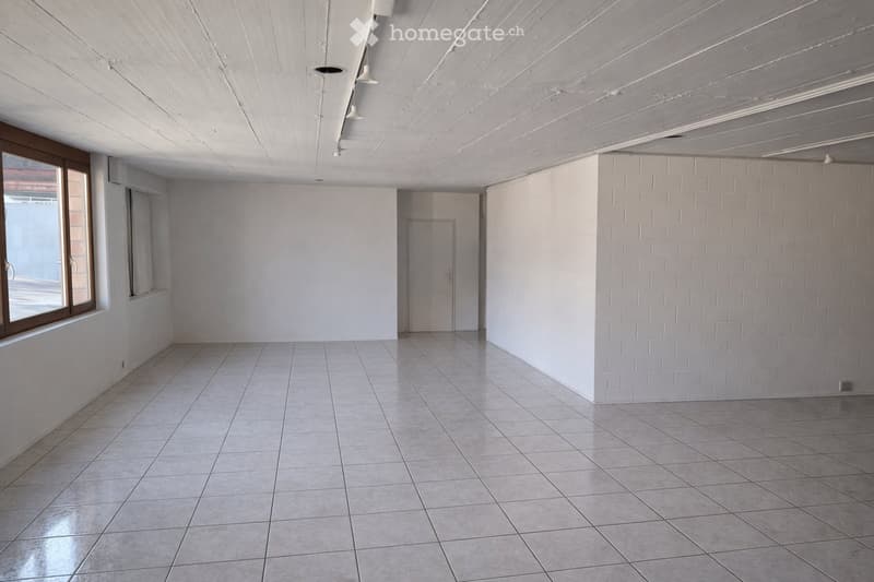 Empty room with tiled floor, white walls, and a single door. The room features a large window on one side and a white brick accent wall on the other.