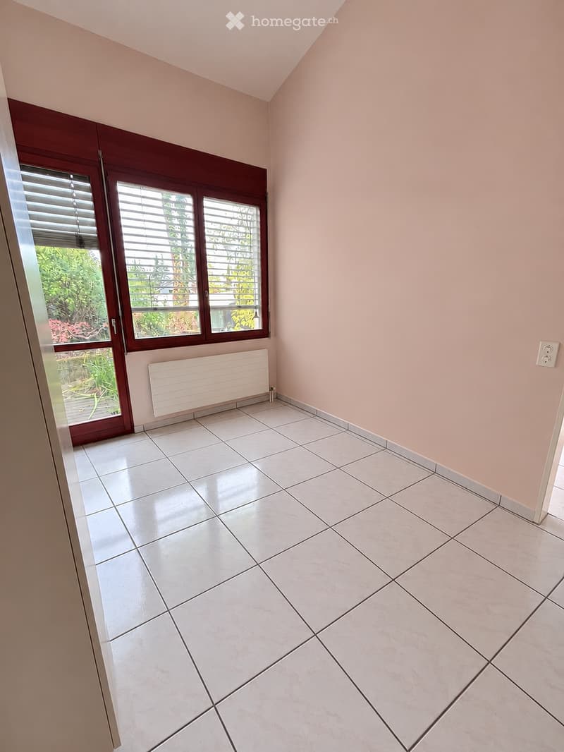 Empty room with light pink walls, white tiled floor, large window with blinds, radiator, and visible electrical outlet.