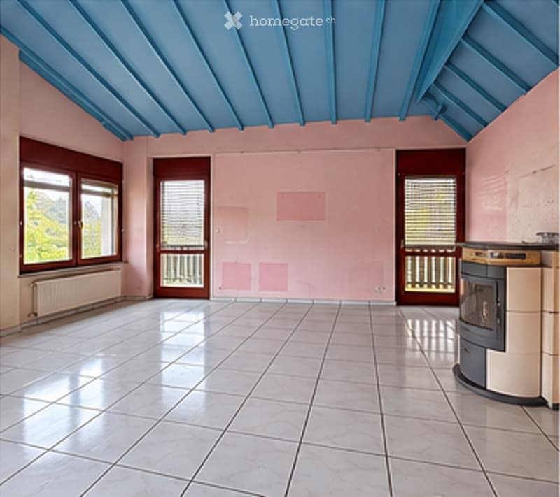 Empty room with light pink walls, white tiled floor, blue ceiling, large windows, and a small balcony area visible through the doors.