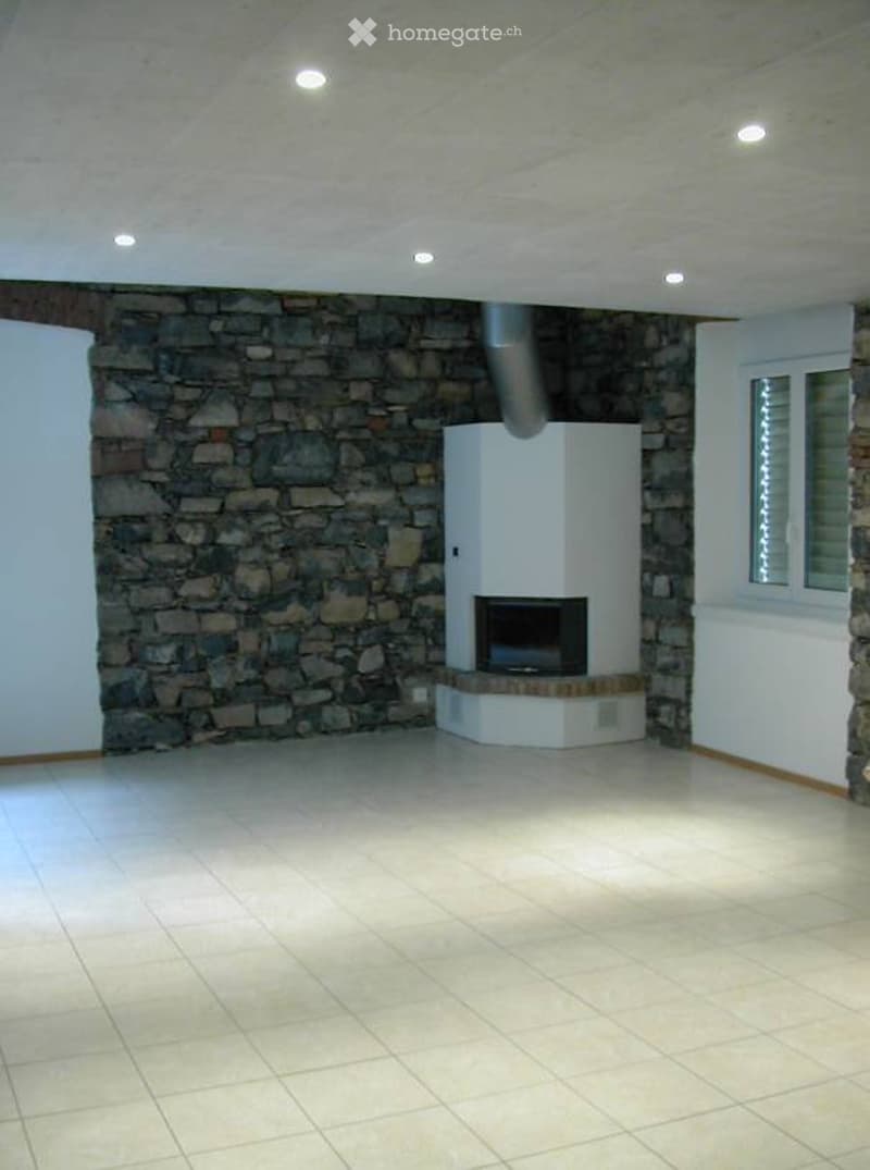Empty room with a stone wall, tiled floor, and a built-in white fireplace unit with a TV screen. No furniture or equipment present.