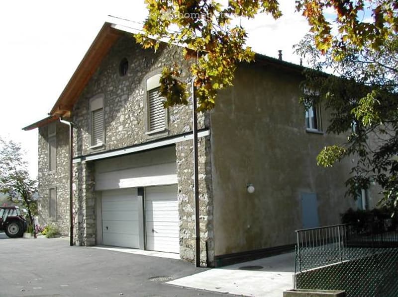 Two-story stone building with a garage entrance, multiple windows, and a sloped roof.