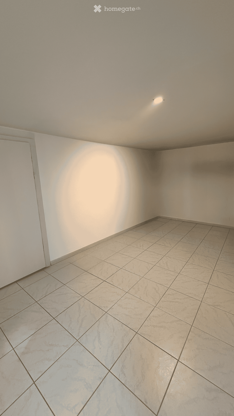 Empty room with beige tiled floor and white walls, featuring a single recessed ceiling light.
