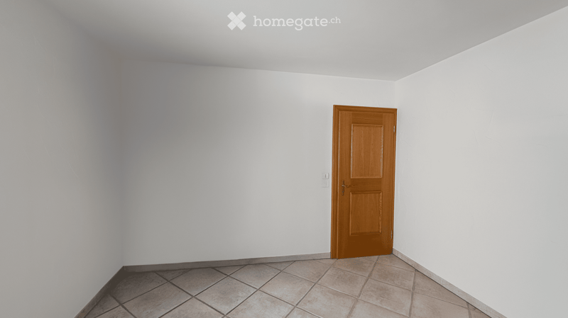 Empty room with white walls, tiled floor, and a single wooden door.