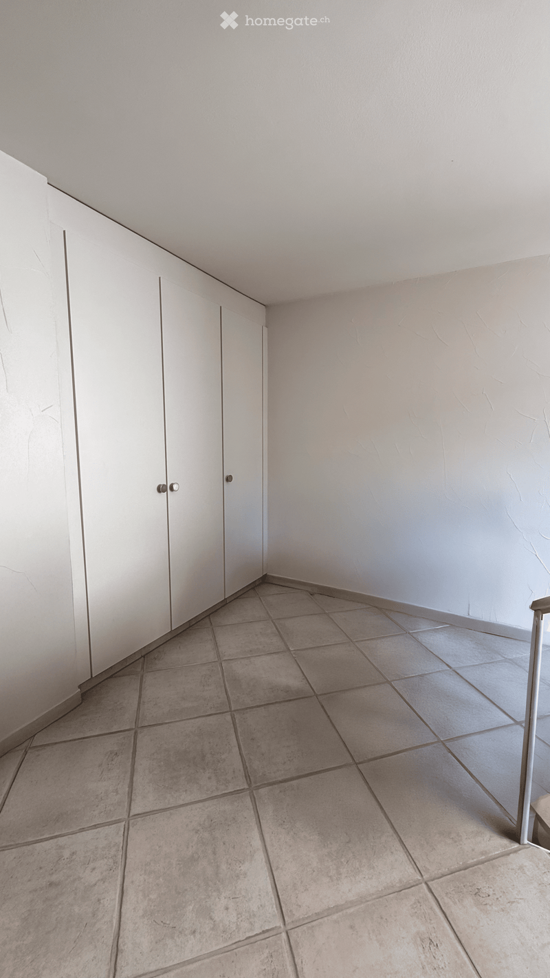 Empty room with tiled floor and white walls, featuring built-in white cabinets on one side.