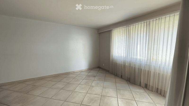 Empty room with tiled floor and light-colored walls, featuring a large window with sheer curtains.