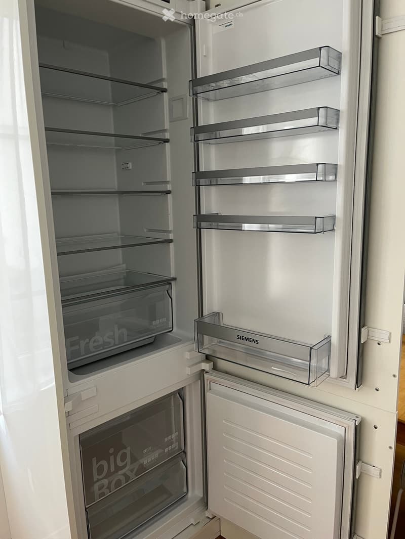 Modern white refrigerator with multiple compartments and shelves, featuring a sleek design and transparent glass doors.