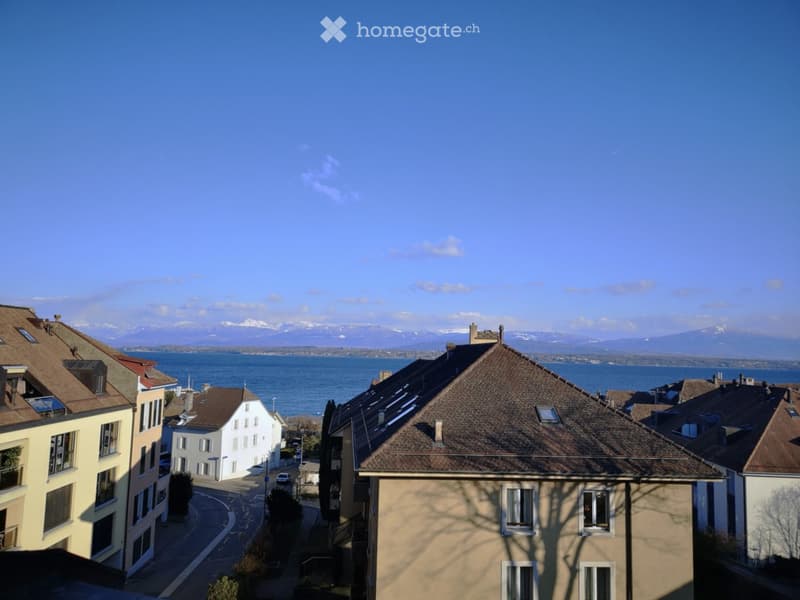 View of a residential street with multi-story buildings, surrounded by a scenic landscape featuring a lake and distant mountains.
