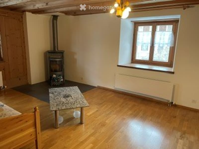 Wooden floor, fireplace, small table, and stool in a cozy room.