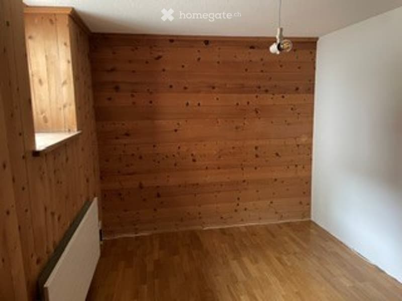 Completely empty room with wooden walls and floor, white wall on one side, radiator, and a window with a wooden frame.
