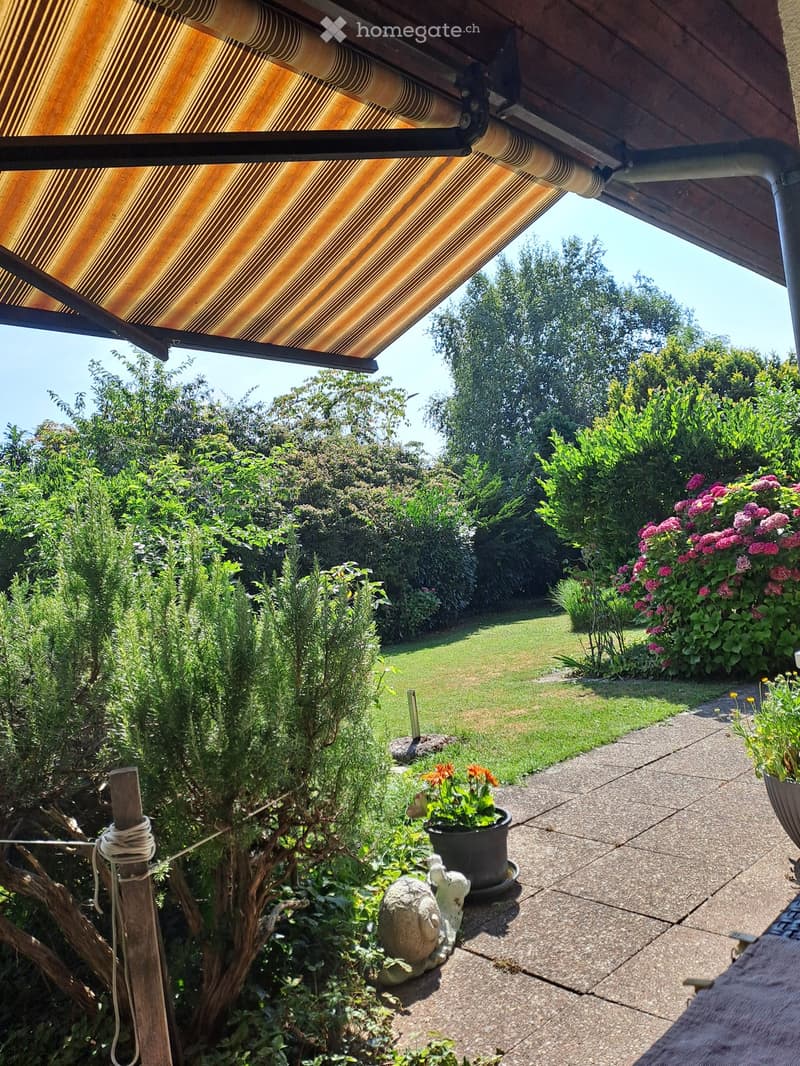 Garden area with a covered patio, potted plants, flowers, and a well-maintained lawn.