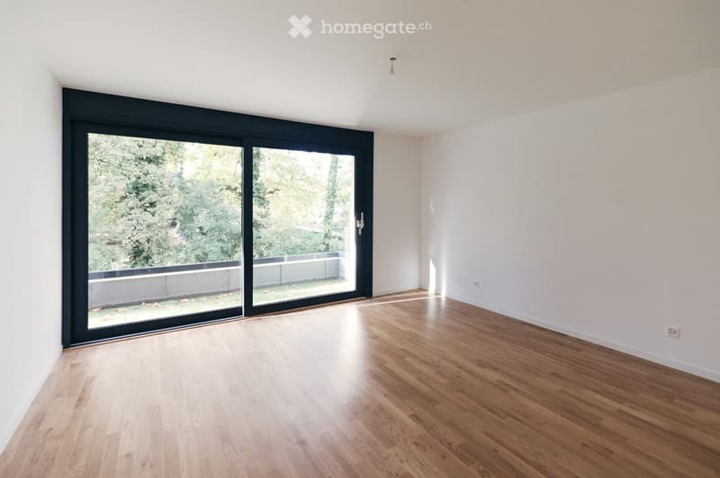 Empty room with light wooden flooring, white walls, and large sliding glass doors leading to a balcony or outdoor area.