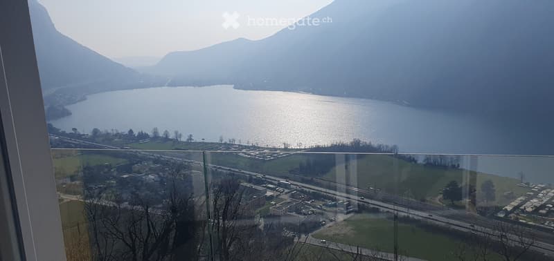 Balcony / Terrace. Balcony with a panoramic view of a lake and surrounding mountains, featuring a modern glass railing and distant town below.