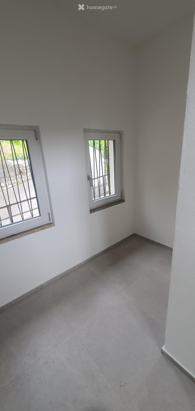 Unfurnished Room. Empty room with white walls, grey tiled floor, and two windows with metal bars.