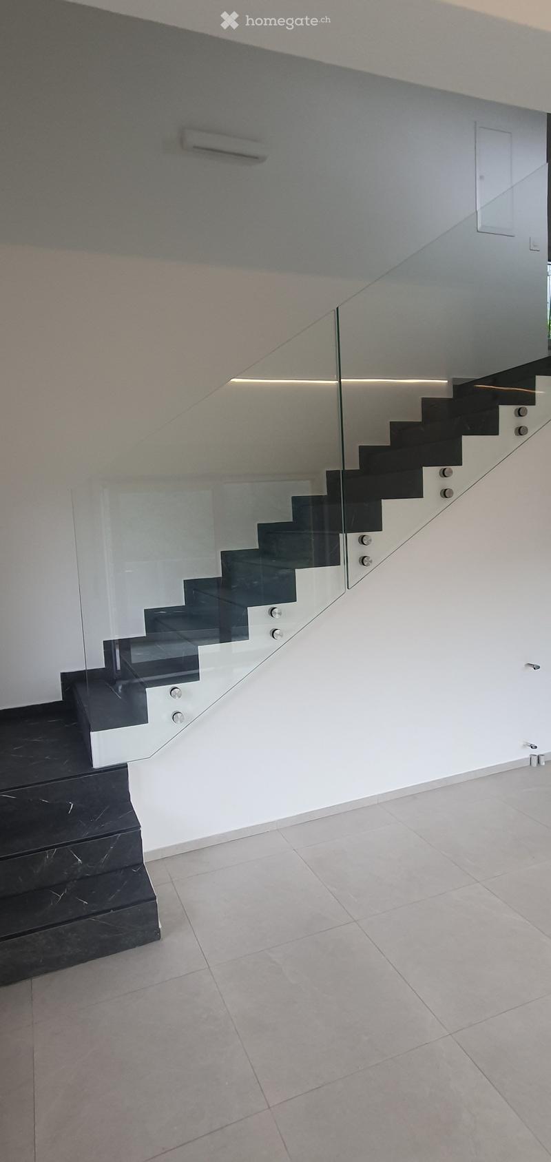 Corridor / Hallway. Modern hallway with a sleek staircase featuring black marble steps and a glass railing, white walls, and tiled flooring.