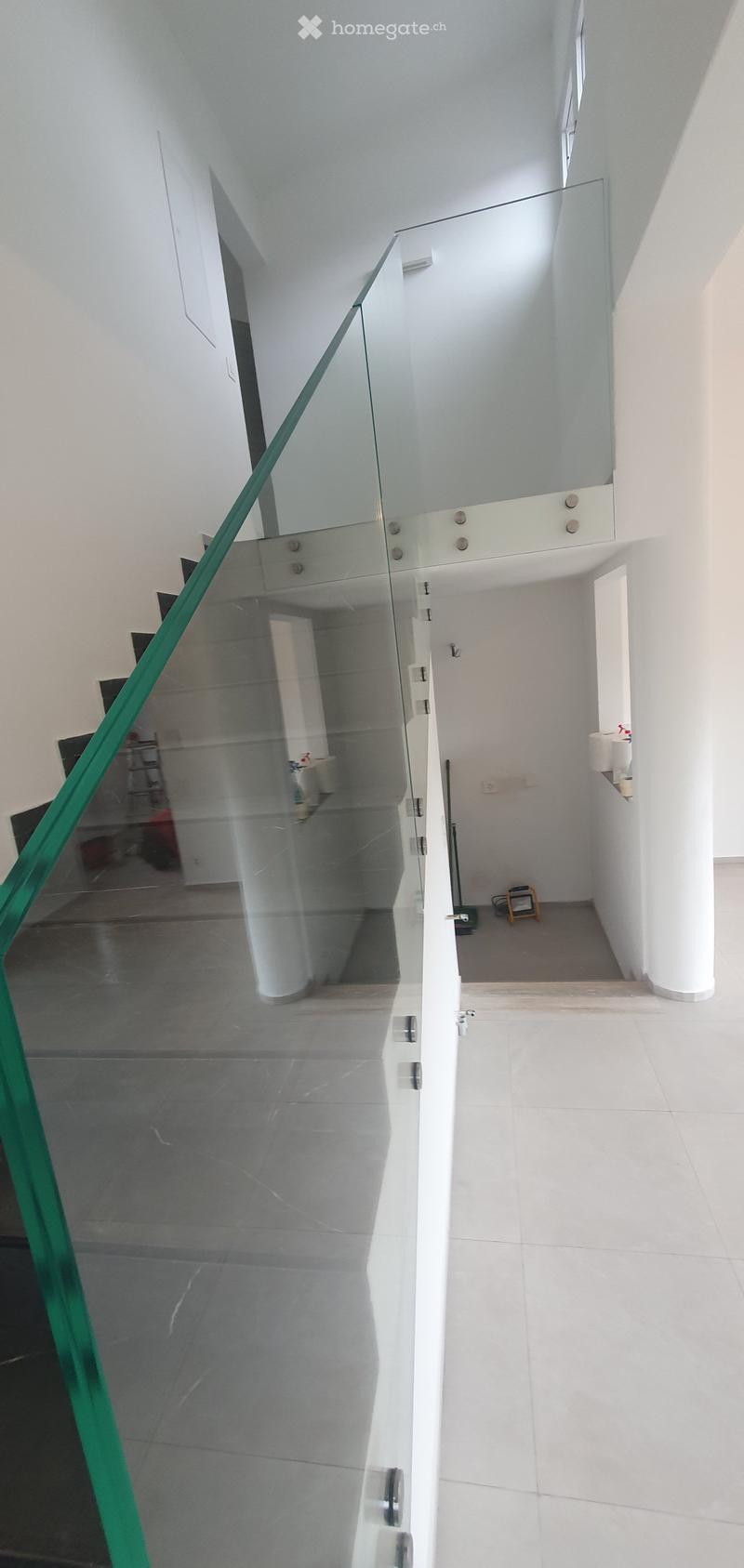 Corridor / Hallway. Modern hallway with white walls, tiled floors, and a glass railing leading to an upper level.