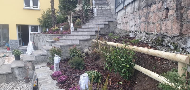 Garden / Outdoor Area. Garden area with stone steps leading up to a house, surrounded by plants and a wooden railing.