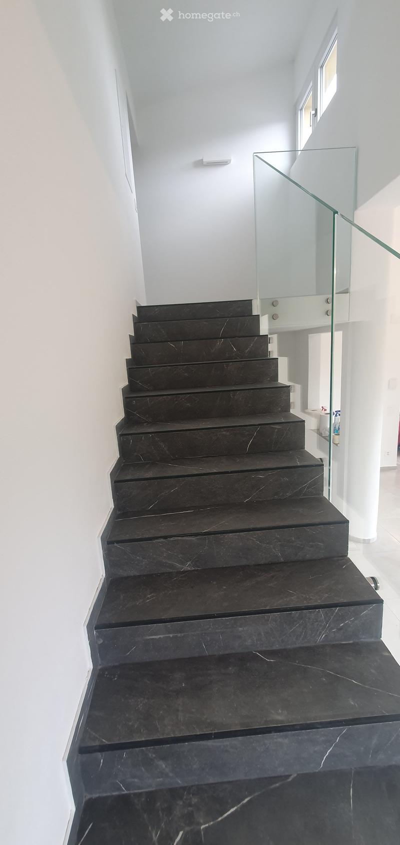 Corridor / Hallway. Modern staircase with black marble steps and a glass railing, leading upwards with white walls and bright lighting.