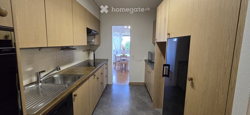 Modern kitchen with wooden cabinets, stainless steel sink, and appliances. Open to a dining area with a table and chairs.