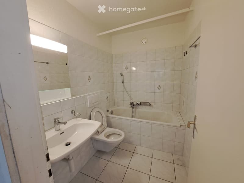 Bathroom with white tiled walls and floor, featuring a sink, toilet, bathtub, and mirror.