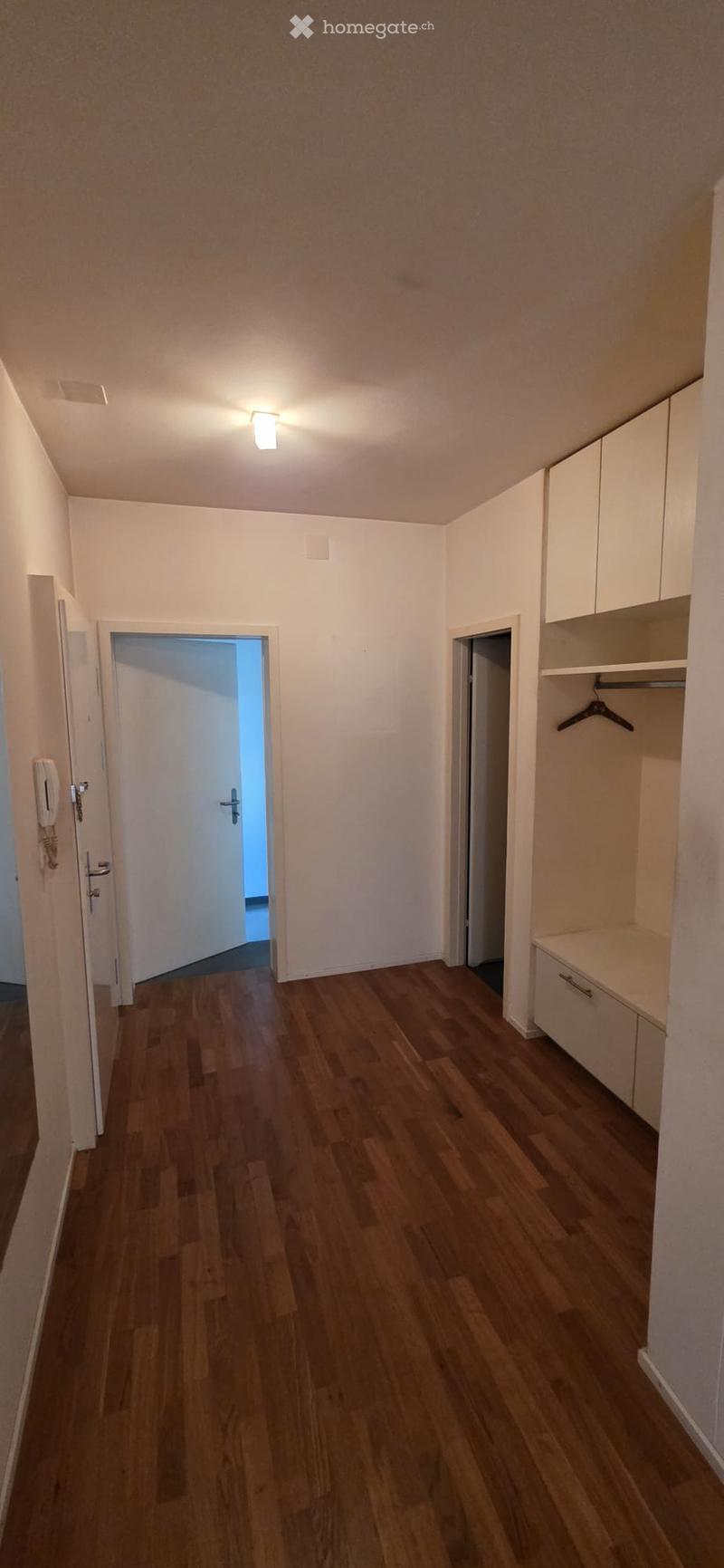 Empty hallway with wooden flooring, white walls, built-in closet with shelves, and two open doors leading to other rooms.
