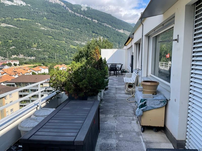Balcony with a view of mountains, featuring a table, chairs, a bench, and potted plants.