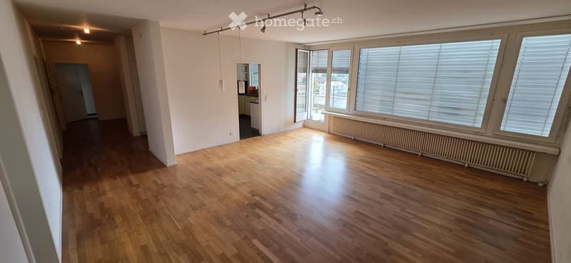 Empty room with wooden flooring, large windows with blinds, and track lighting. No furniture or equipment visible.