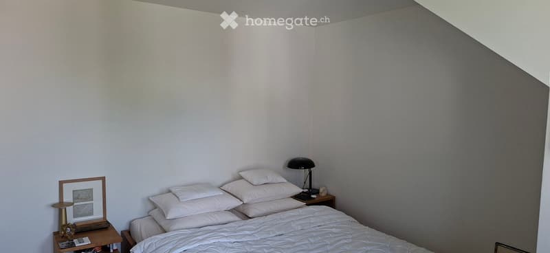 A modern bedroom with a neatly made bed, nightstand, lamp, and picture frame on a side table.