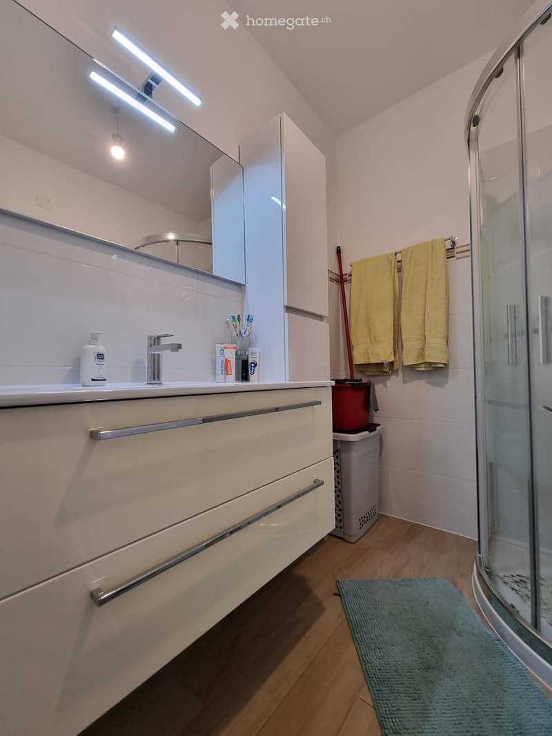 modern bathroom with white cabinets, silver faucet, mirror, glass shower, wooden floor, yellow towels, cleaning supplies