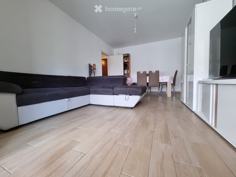 modern living room with a large L-shaped sofa, wooden floor, white walls, dining table, and a TV