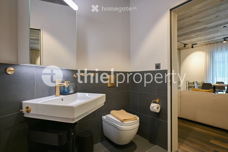 Modern bathroom, white sink, modern fixtures, tiled walls, white toilet, towel on the toilet