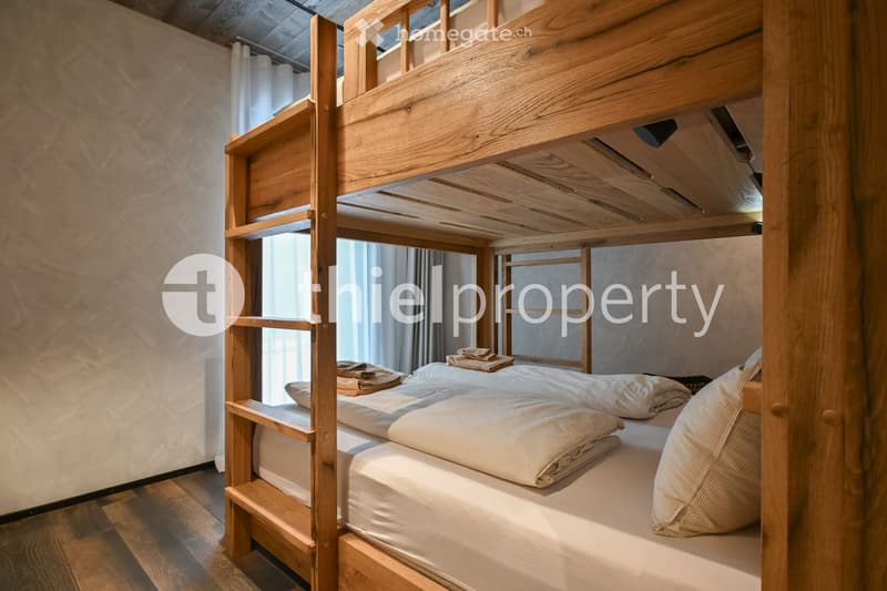 Three-tiered bunk beds, wooden headboards, white linens, wall hanging, wooden flooring