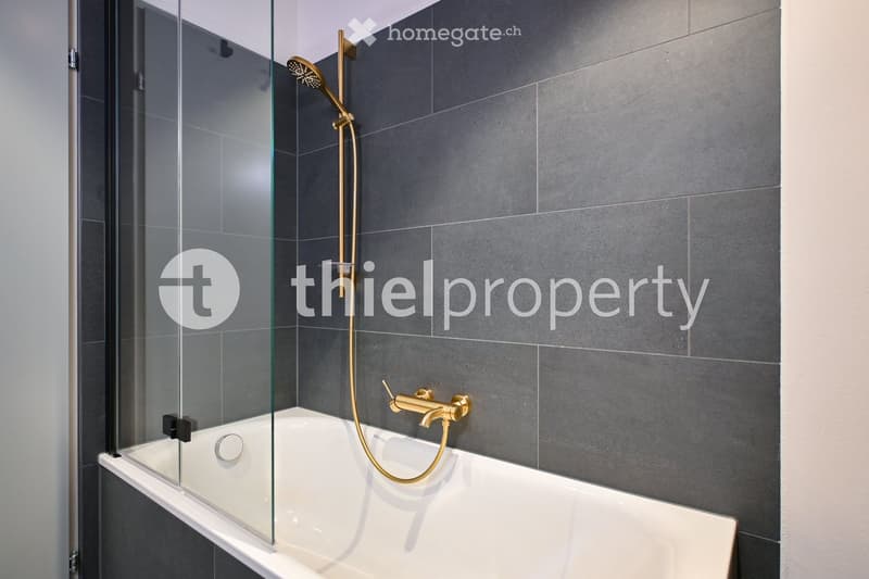 Shower, bathtub, grey tiles, golden fixtures, glass door