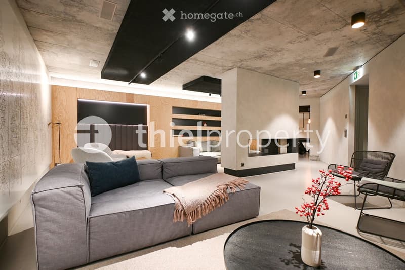 L-shaped grey sofa, black round table with flower vase, grey chairs, fireplace with shelves, wooden panels, beige rug