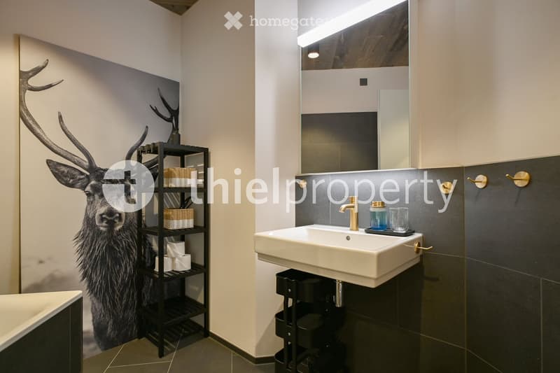 Bathroom: large white sink, black shelf with decorative items, modern mirror with light, black and white wallpaper, tub.