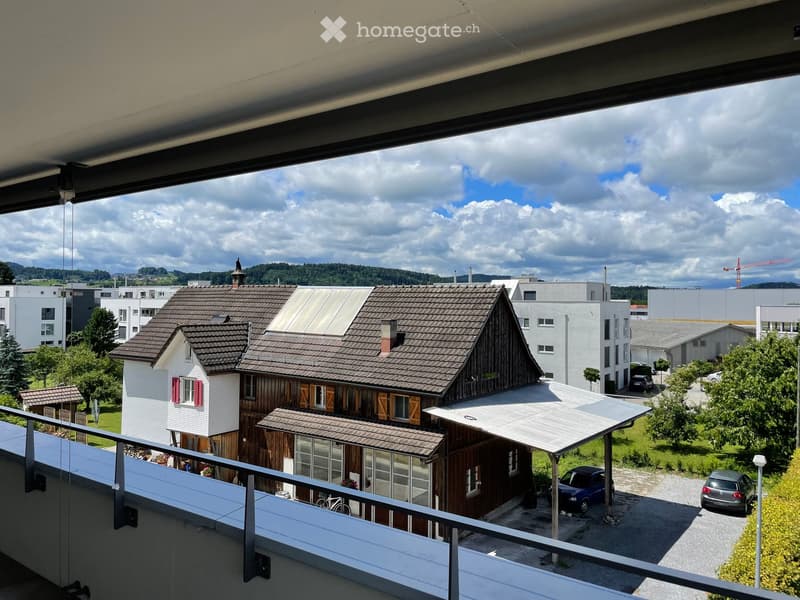 Balcony overlooking a residential area with houses, trees, and a partly cloudy sky.