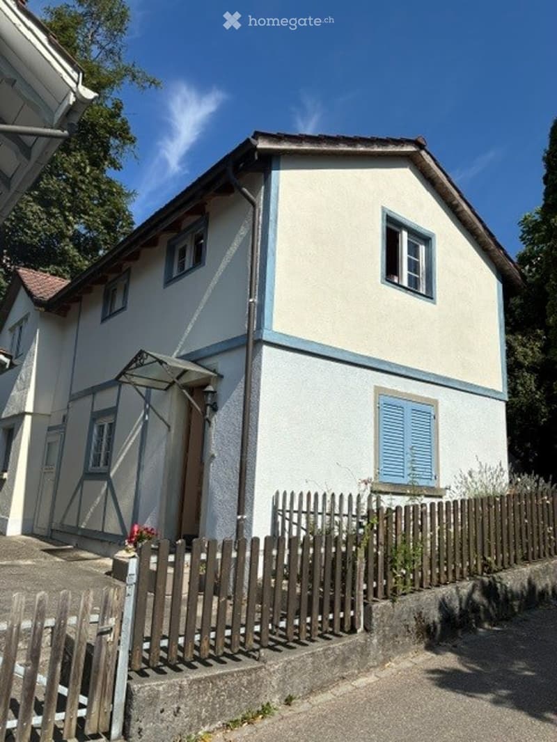 Two-story house with white siding, blue shutters, and a wooden fence in front.