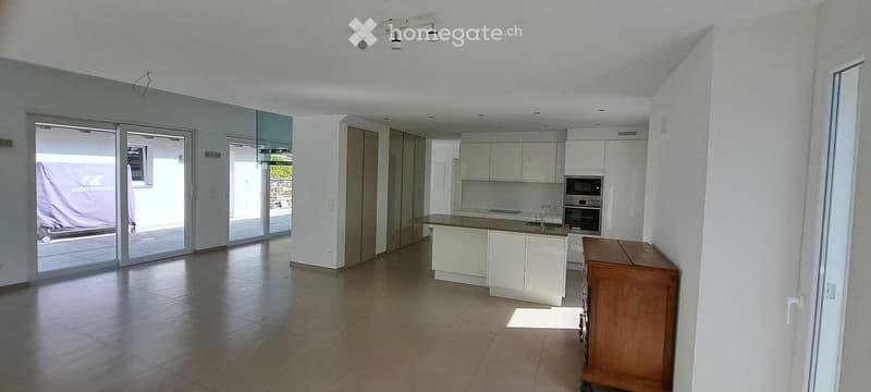 Modern kitchen with white cabinets, a central island, and built-in appliances including an oven and microwave. The space features large sliding glass doors leading to an outdoor area.